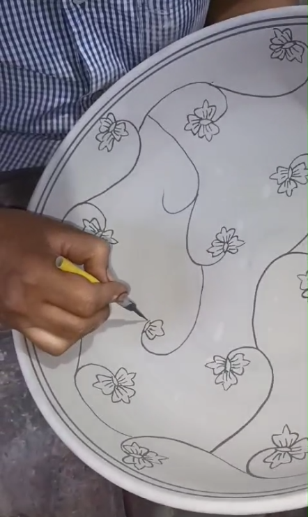 Artisan traçant un motif floral sur une assiette