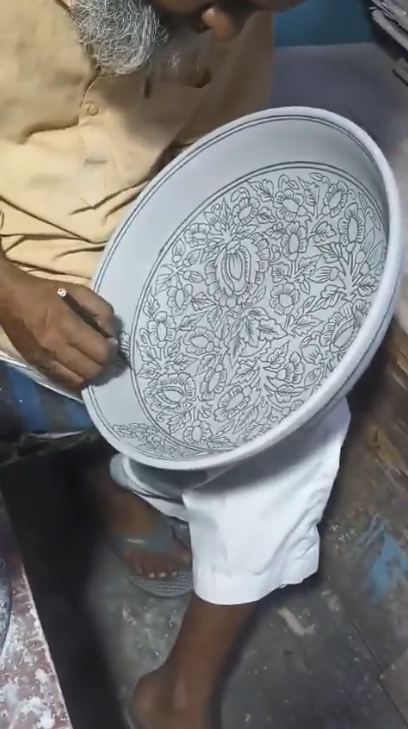 Artisan dessinant les ornements d'une grande assiette